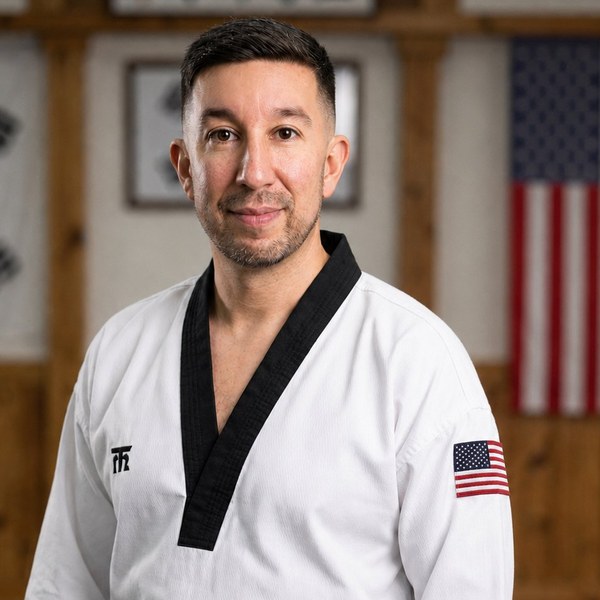 Head Instructor of Rank Up Martial Arts in his Taekwondo dobok with the Korean and American flags behind him